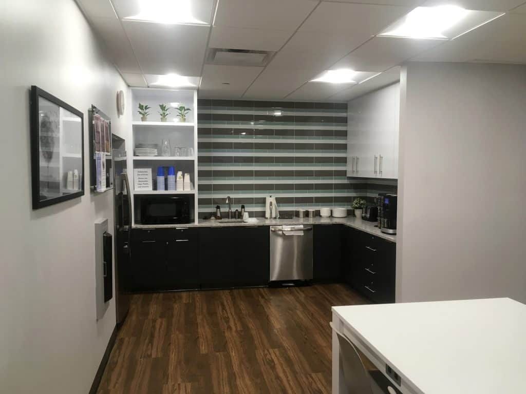 Modern kitchen with dark cabinets, stainless dishwasher, white countertops, and wood floors