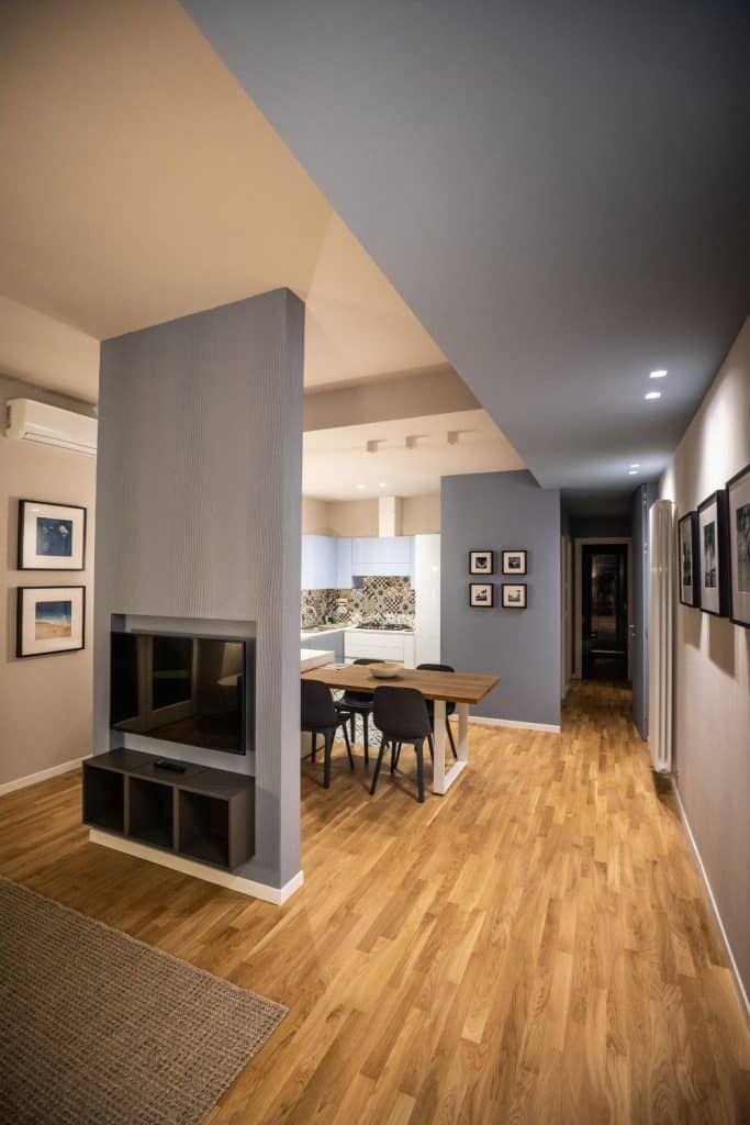 Modern open living room with wooden floors, gray fireplace column, and dining table under recessed lighting