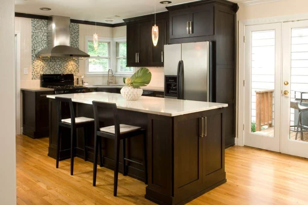 Modern kitchen with dark cabinets, stainless steel appliances, white island, and three black barstools