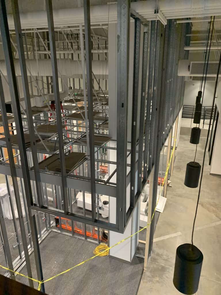 Interior of a steel-framed construction site with hanging black fixtures and exposed wiring
