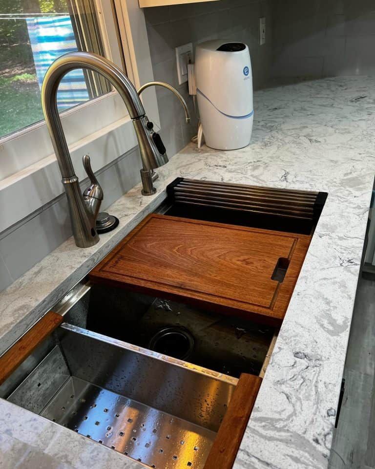 Kitchen sink with wooden cutting board covers and a pull-down faucet on a marble countertop.
