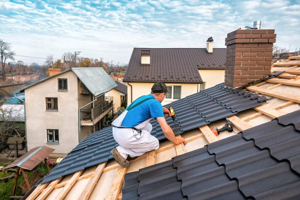 Worker installing dark roof tiles on a house roof under a blue sky