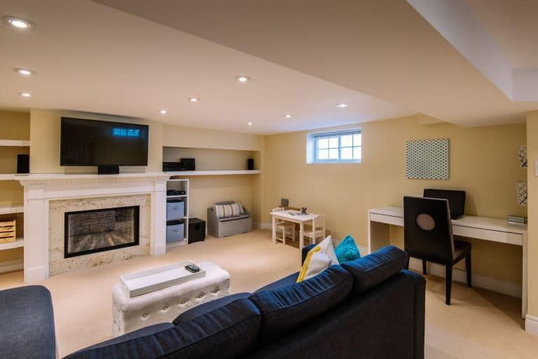 Cozy finished basement with fireplace, TV, sofa, desk, and small window in a beige room