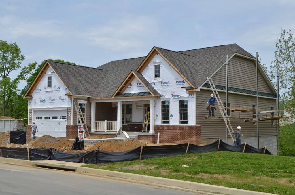 New house under construction with workers, white siding, and black erosion fencing along the front yard