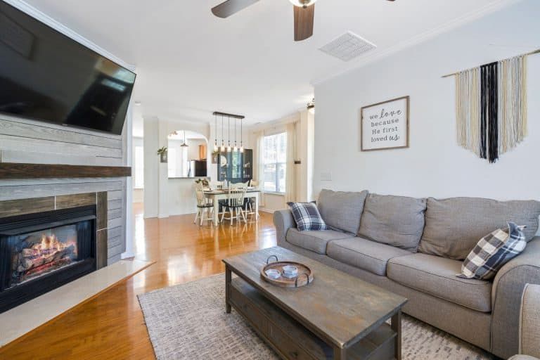 Modern living room with gray sofa, fireplace, wall art, and open dining area with hardwood floors