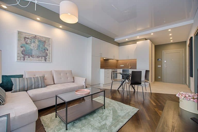 Bright modern living room with sectional sofa, coffee table, dining area, and kitchen in the background