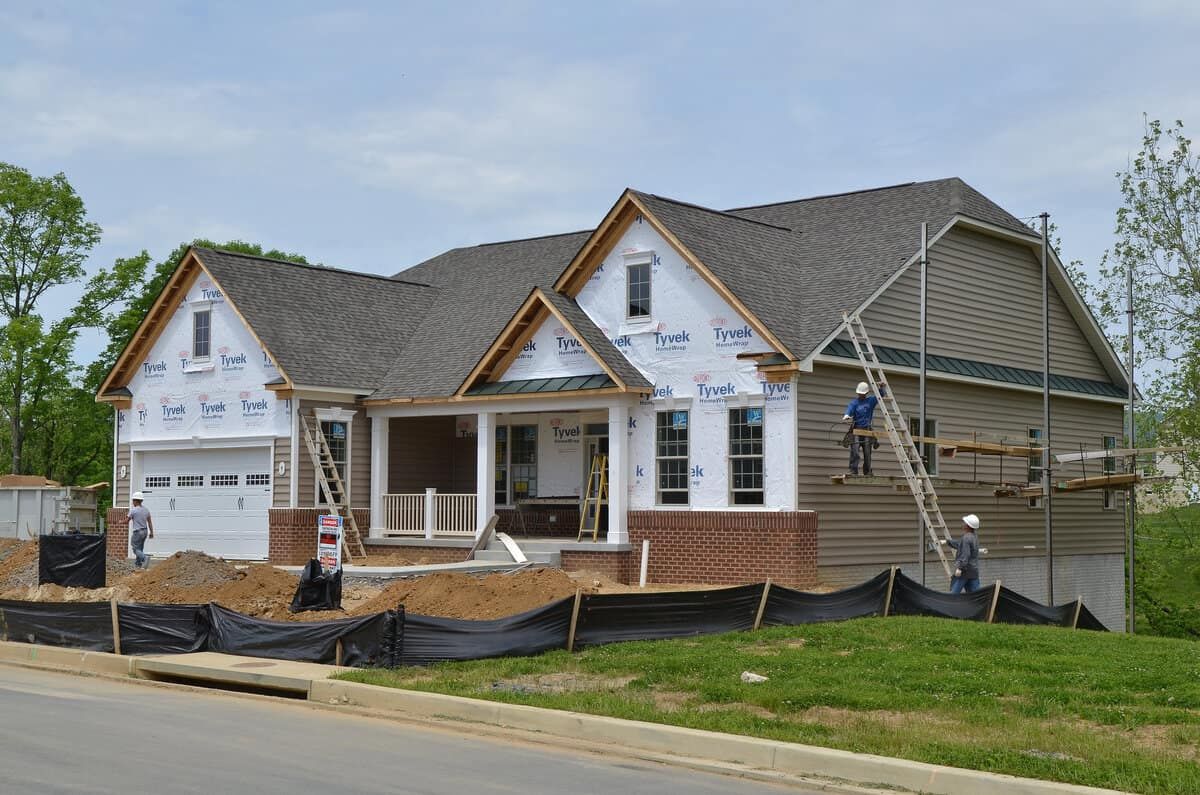 Partially built suburban house with white siding, gray roof, and construction materials in front