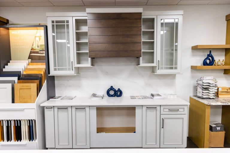 Modern kitchen display with white cabinets, wood accent panels, and open shelving holding decor and dishes