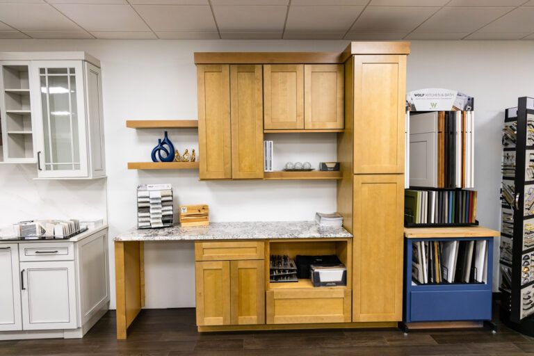 Kitchen display of wooden cabinets, white sink, and shelving with stacked books and a stainless steel fridge