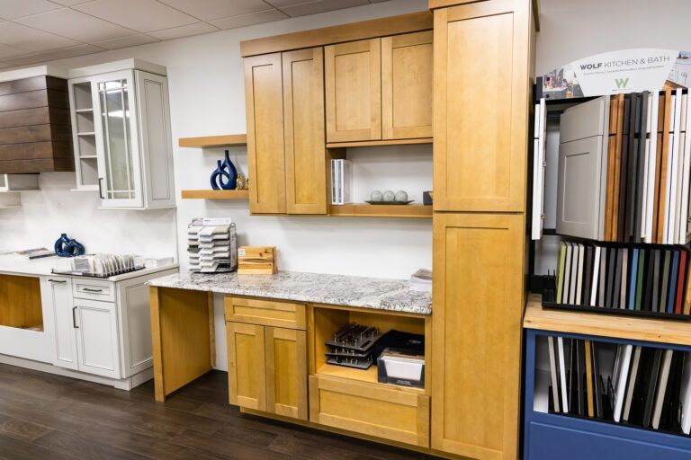 Kitchen showroom with light wood cabinets, white countertops, and a display rack of cabinet finishes on the right
