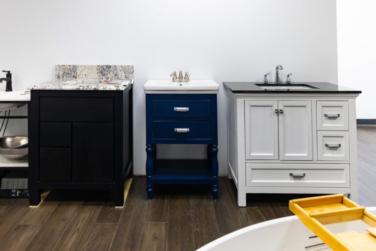 Three bathroom vanities in black, blue, and white on a dark wood floor.
