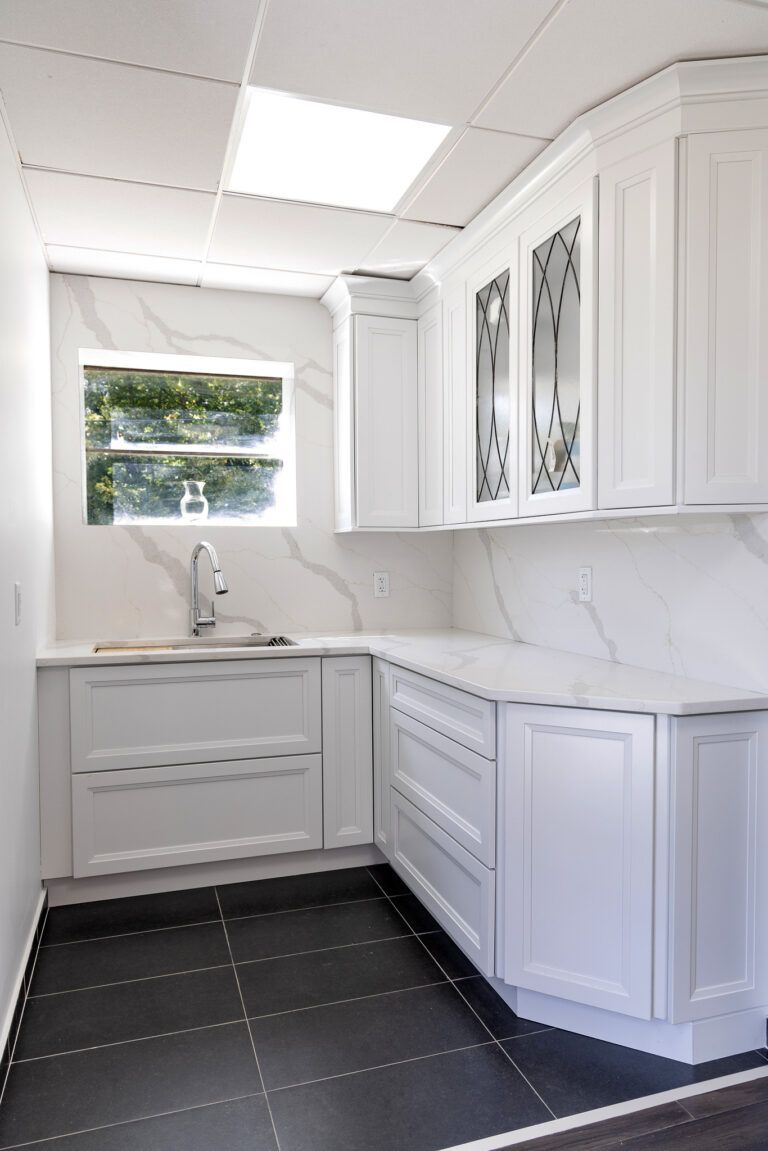 Bright white kitchen with marble counters, glass cabinets, and a window over the sink
