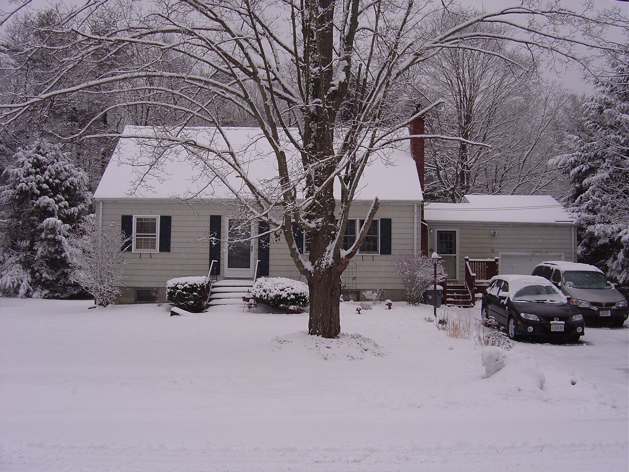 A snowy house with cars parked in front of it