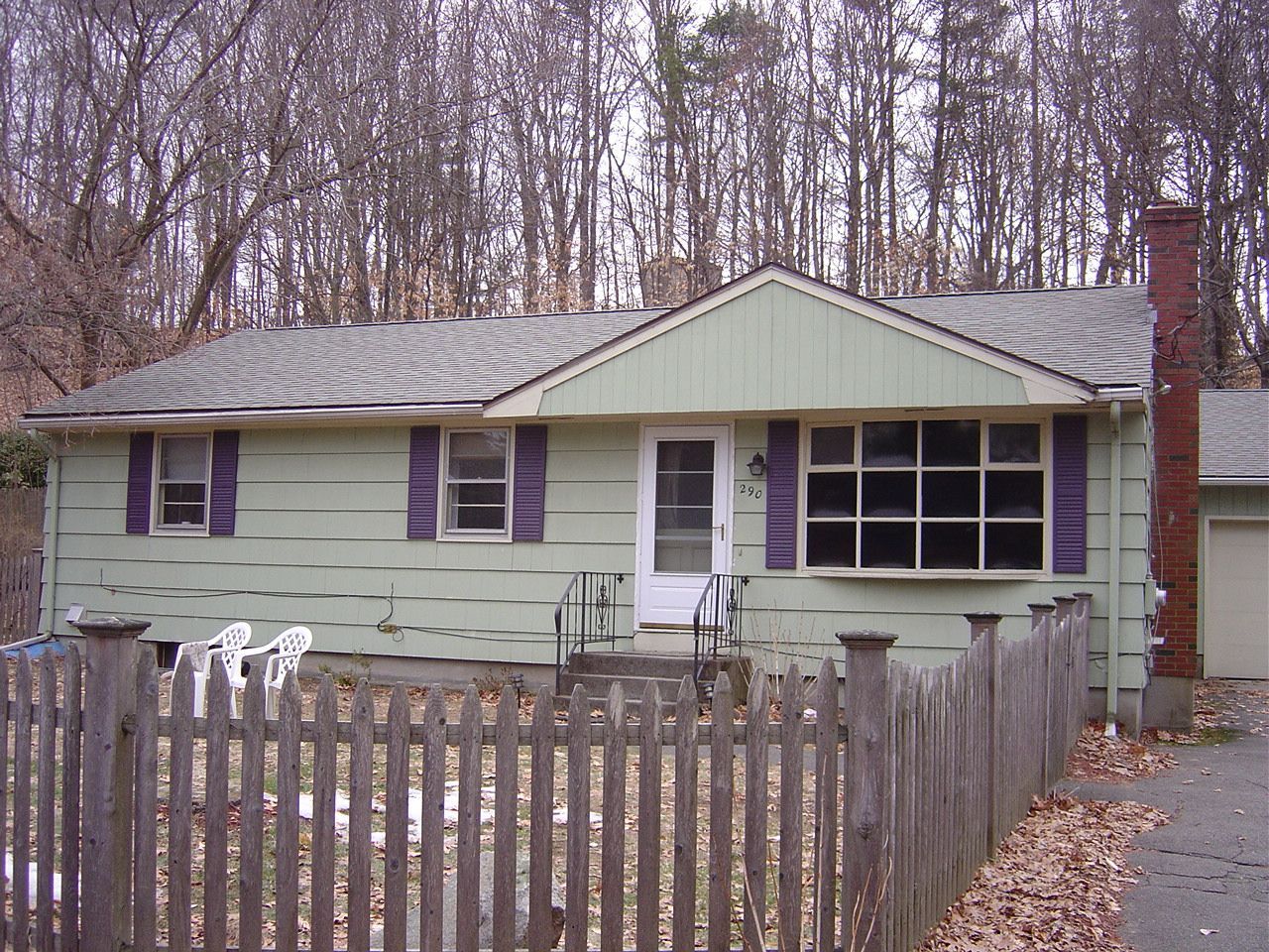 A green house with purple shutters and a picket fence