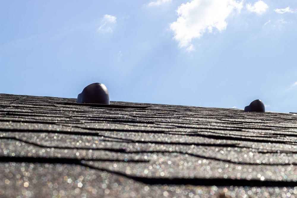 Black shingle roof with two dark vents against a blue sky with scattered clouds.