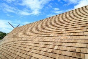 Wooden shingle roof against a blue sky with clouds.
