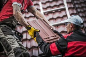 Two roofers exchanging roof tiles on a sloped roof.