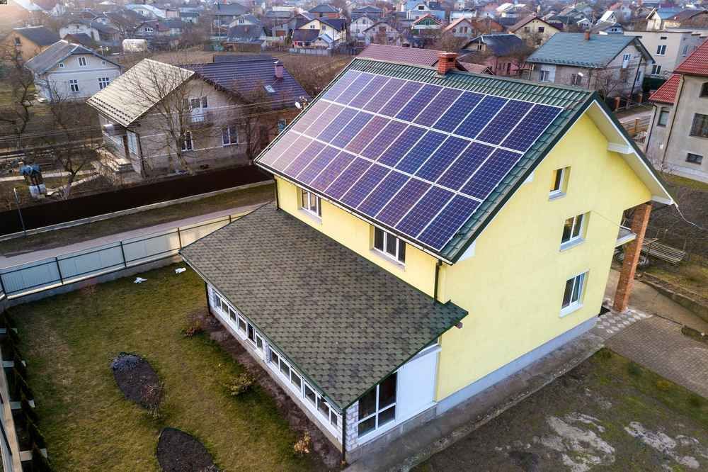 Yellow house with solar panels on the roof; other houses in background.
