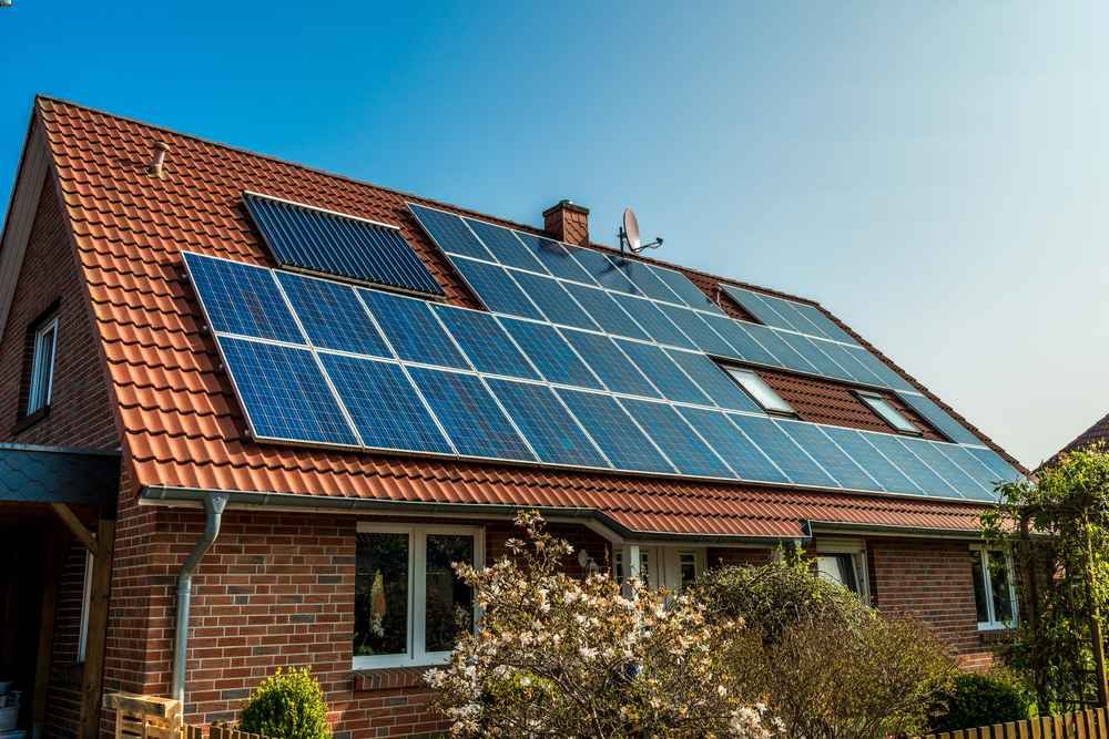 Solar panels on the red-tiled roof of a brick house under a blue sky.