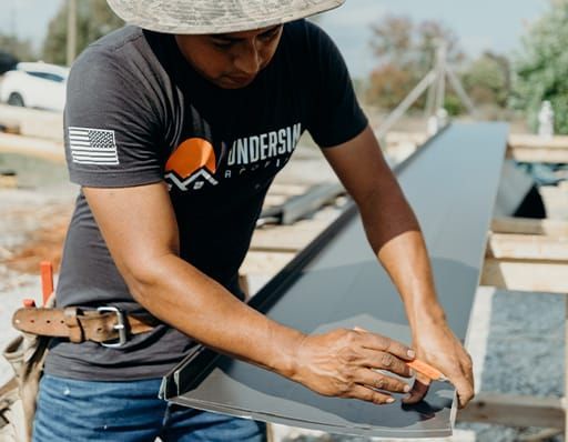 Construction worker shaping metal flashing outdoors.