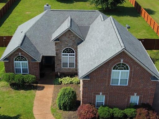 Brick house with gray roof, arched windows, and manicured landscaping in a suburban setting.