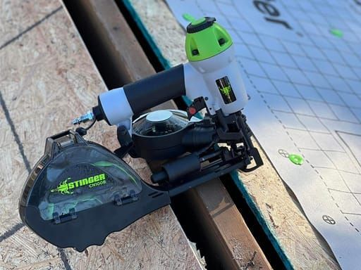 Stinger nail gun on wood, beside roofing material; green and black colors; outdoors.