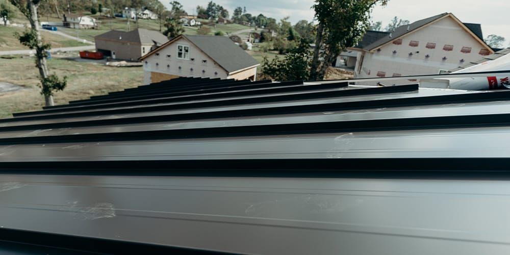 Metal roof installation with houses in the background.