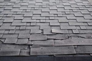 Gray asphalt shingles on a roof, some damaged and lifting.