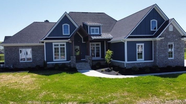Blue and gray house with black roof, brick facade, and green lawn under a clear sky.