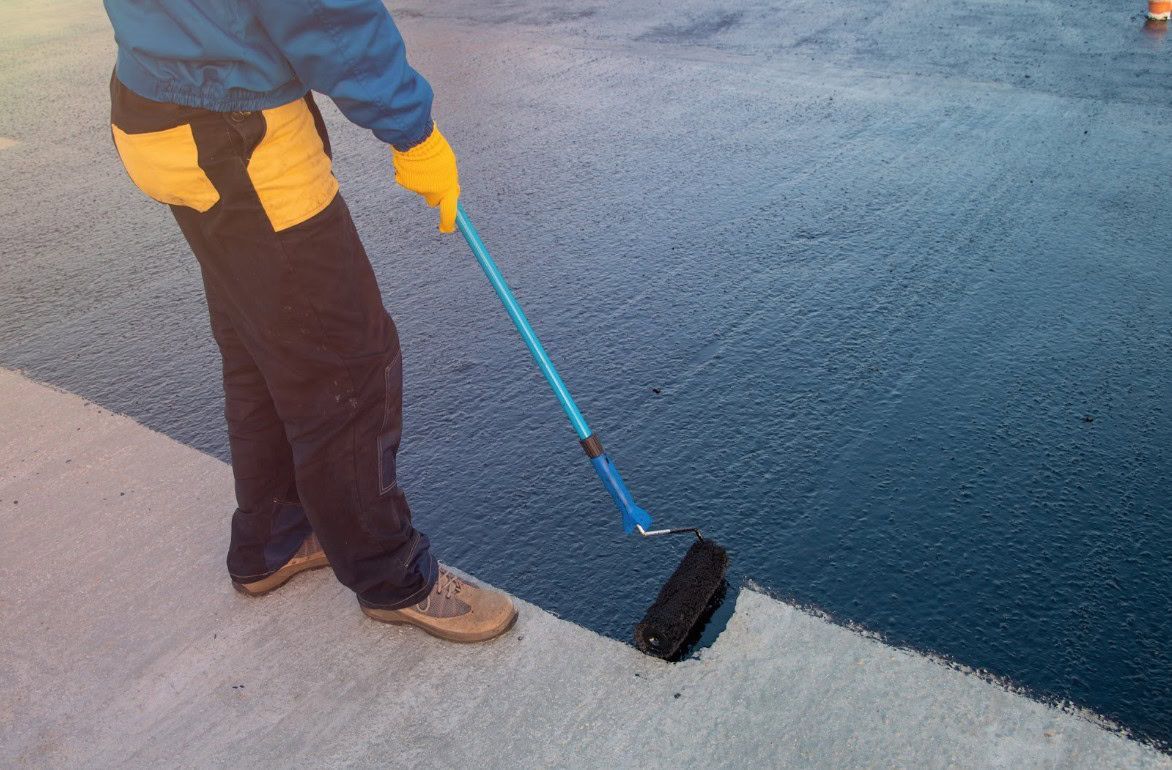 Person applying blue sealant to a concrete surface with a roller.