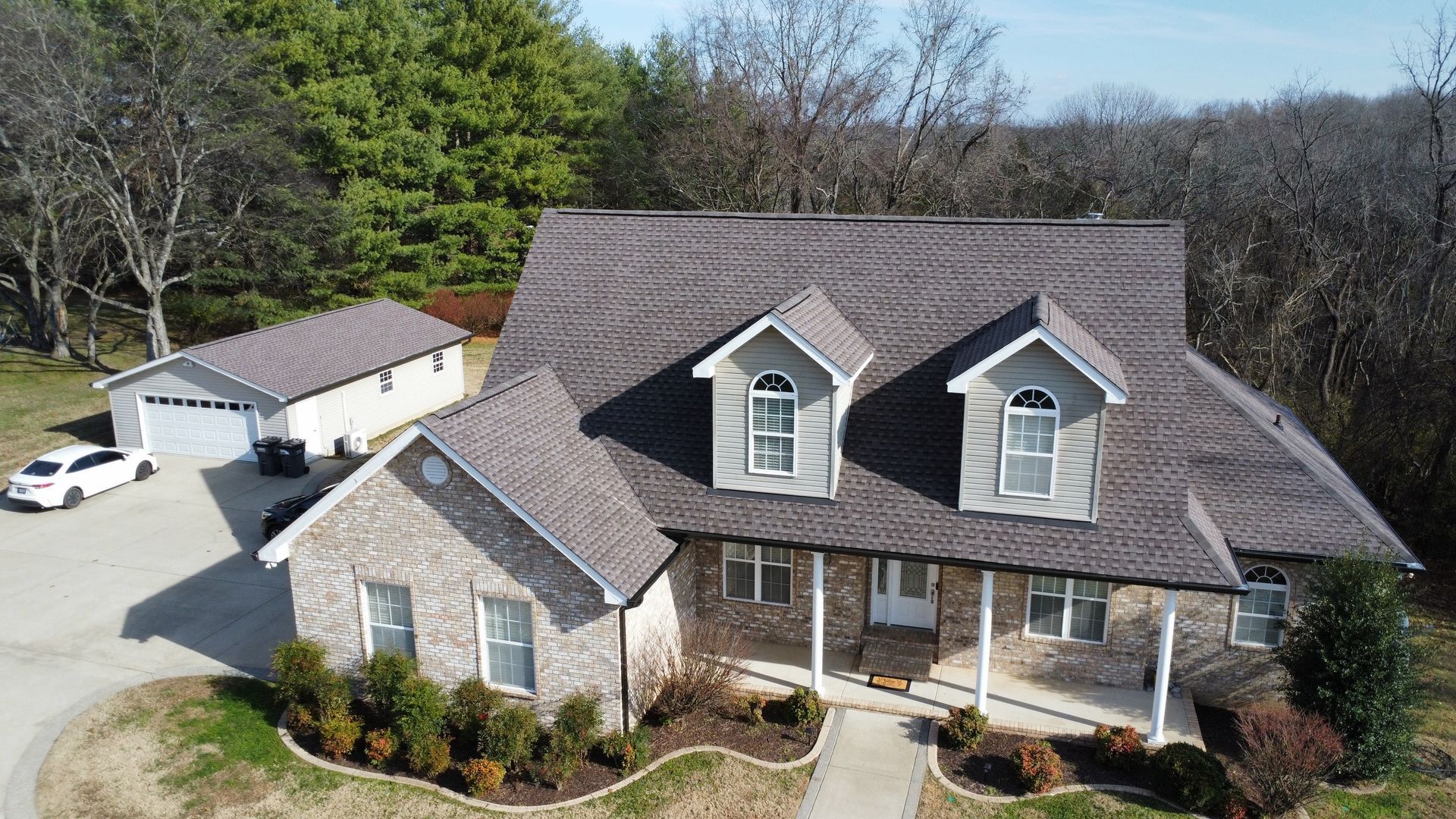 Aerial view of a large suburban house with a driveway, front porch, and surrounding trees.