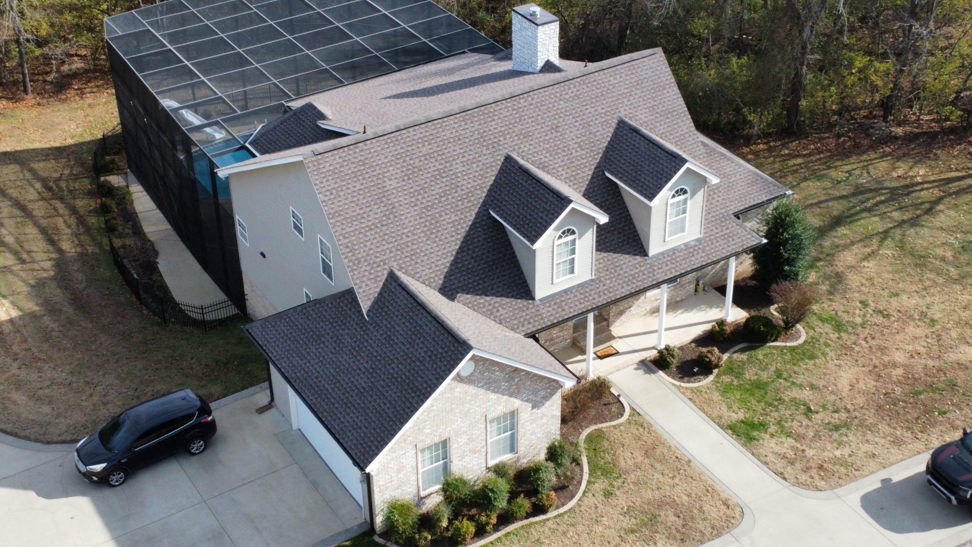 Aerial view of a house with solar panels, driveway, and a parked black car on a suburban lot