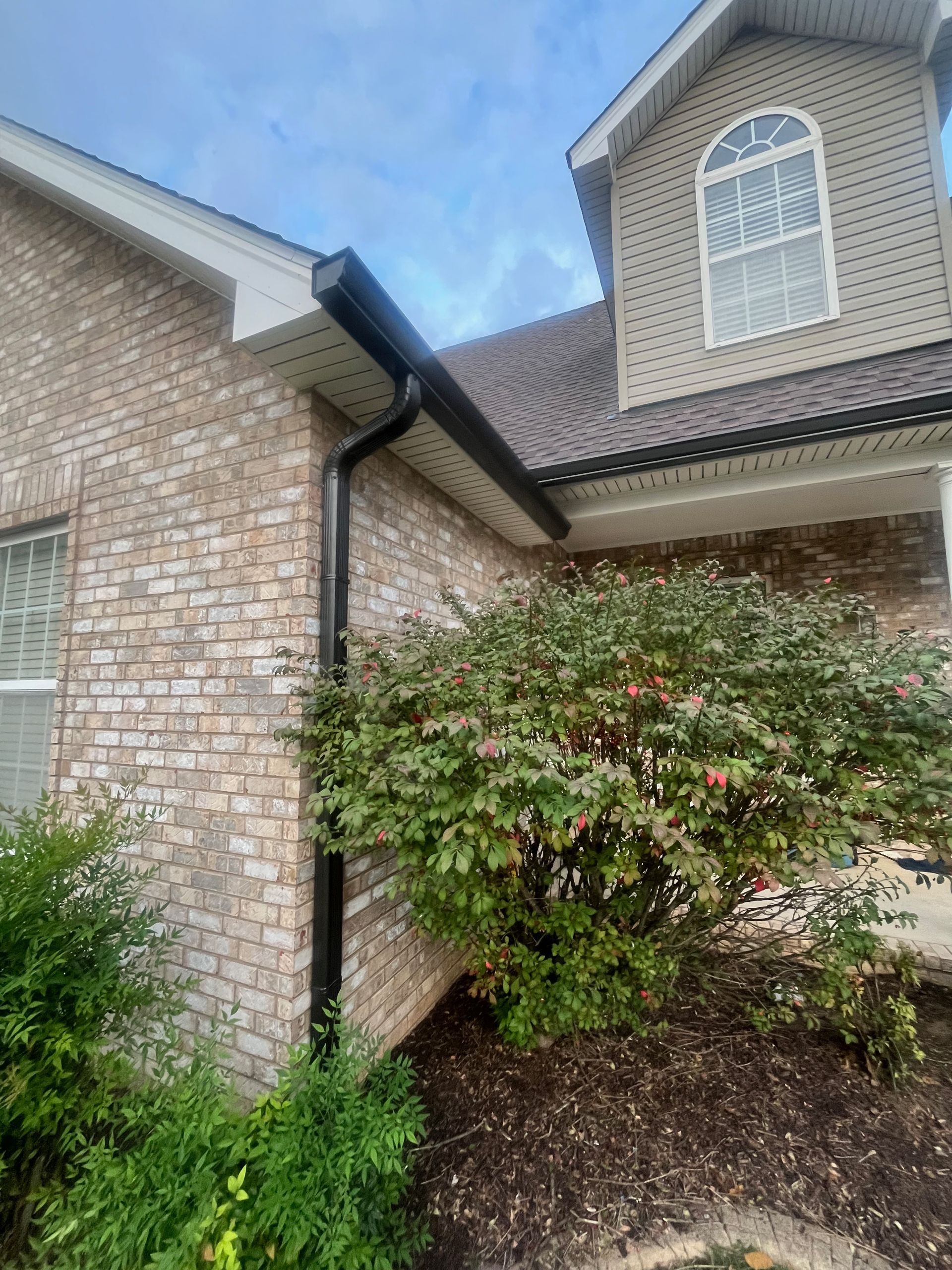 Brick house exterior with white-trim windows, black gutter, and green shrubs by the entrance