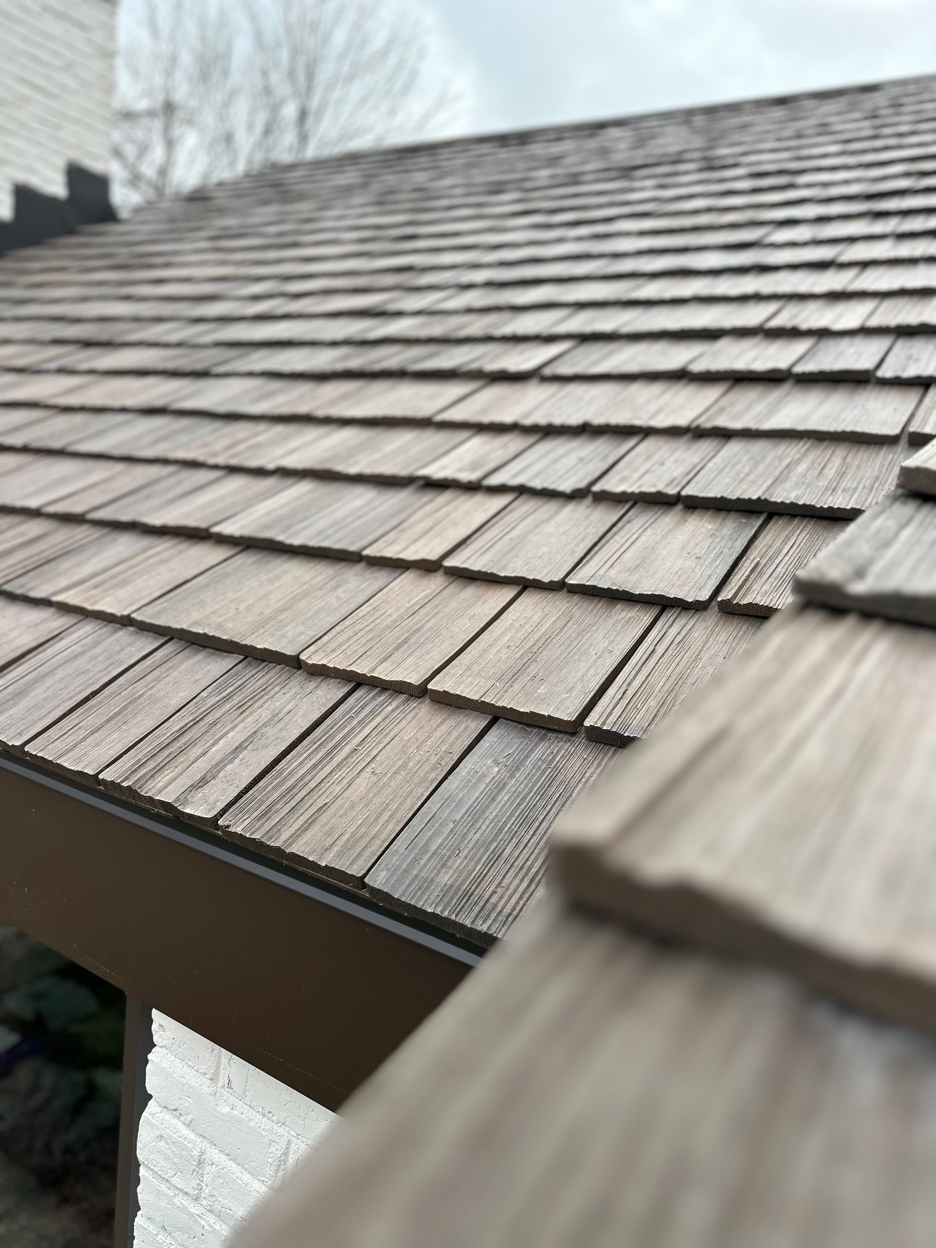 Close-up of a shingled roof with weathered gray-brown wooden shingles and a blurry background sky