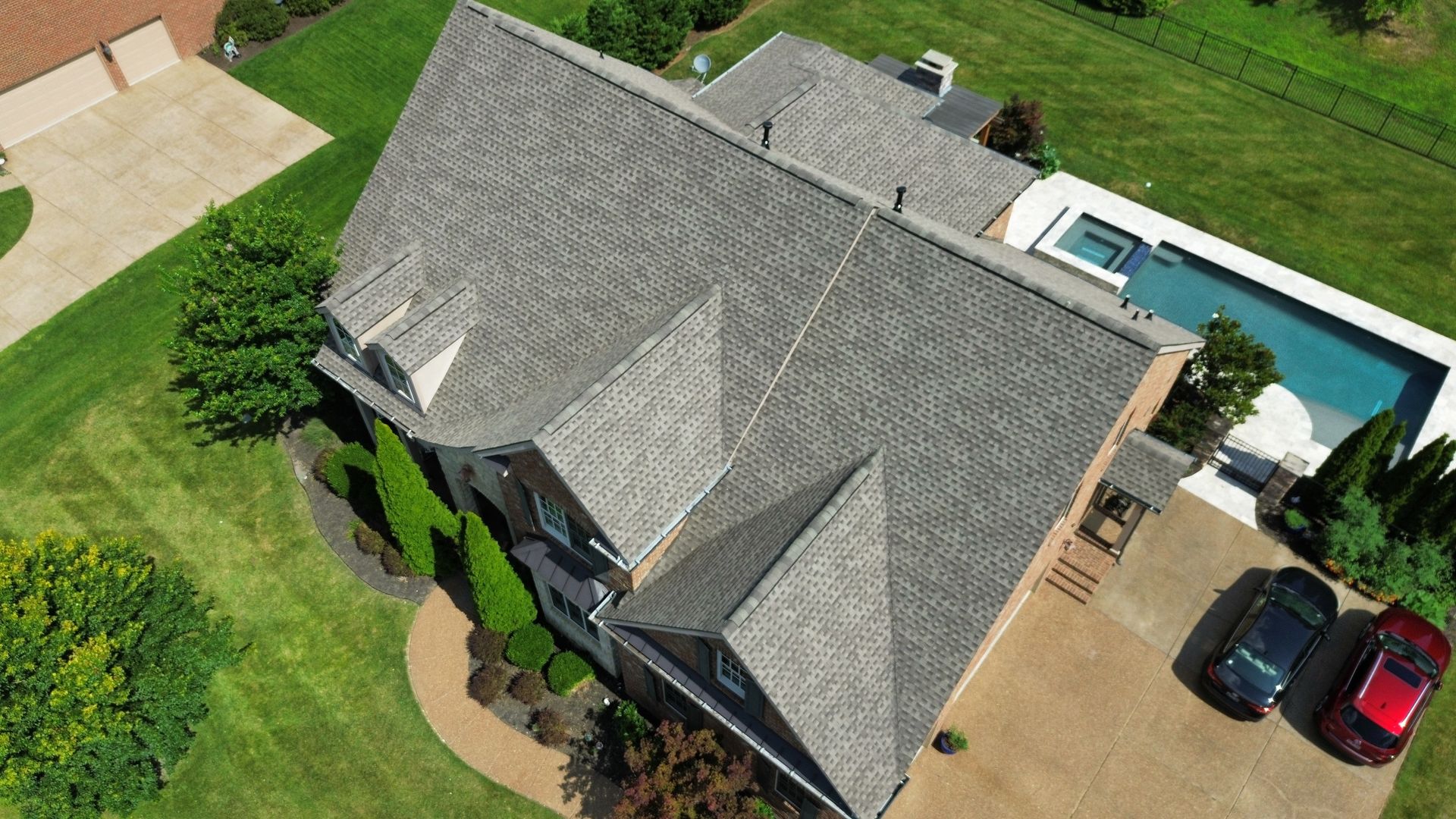 Aerial view of a house with gray roof, driveway, two cars, and a backyard pool.