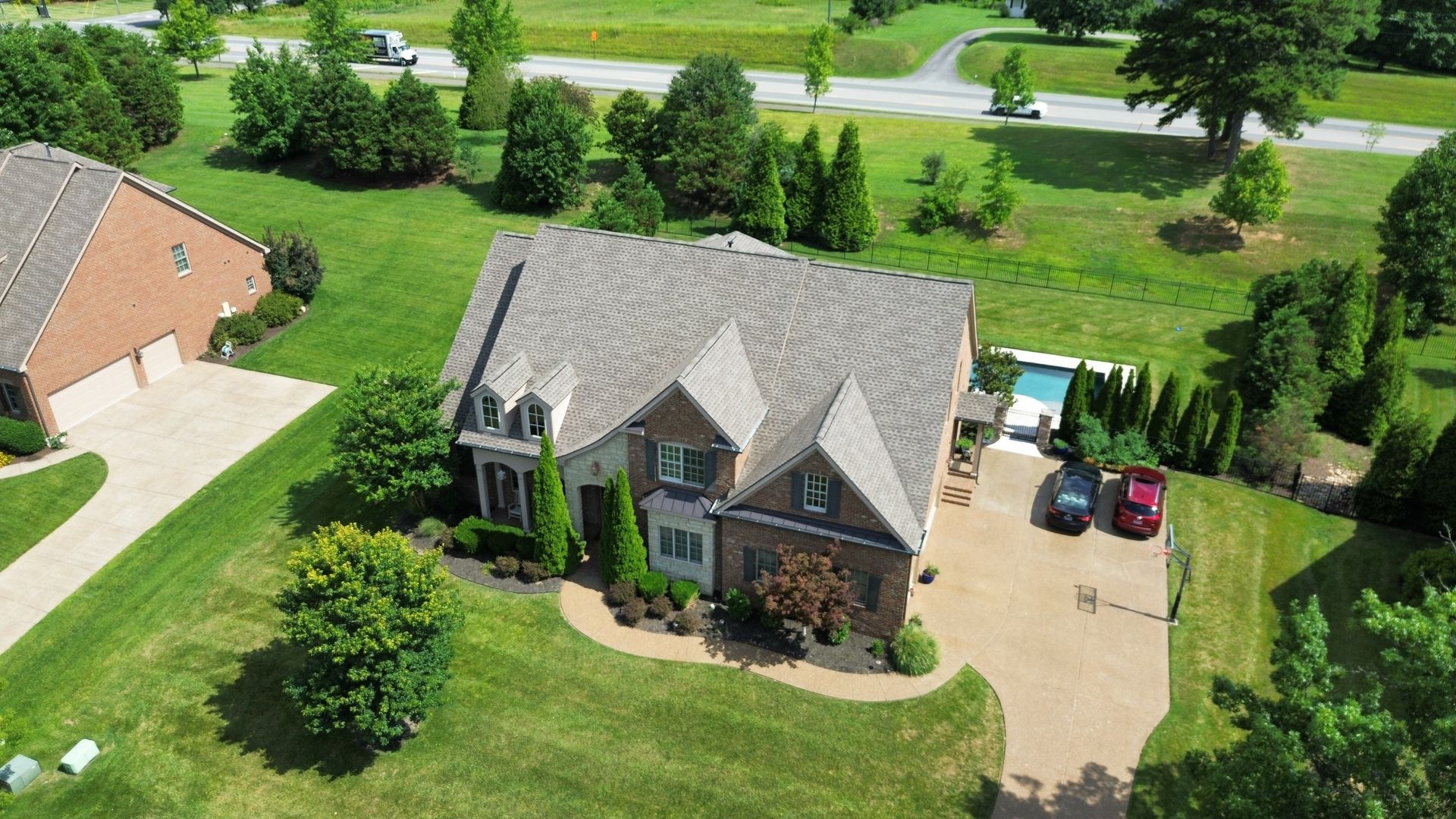 Aerial view of a gray-roofed suburban house with a driveway, green lawn, and parked car.