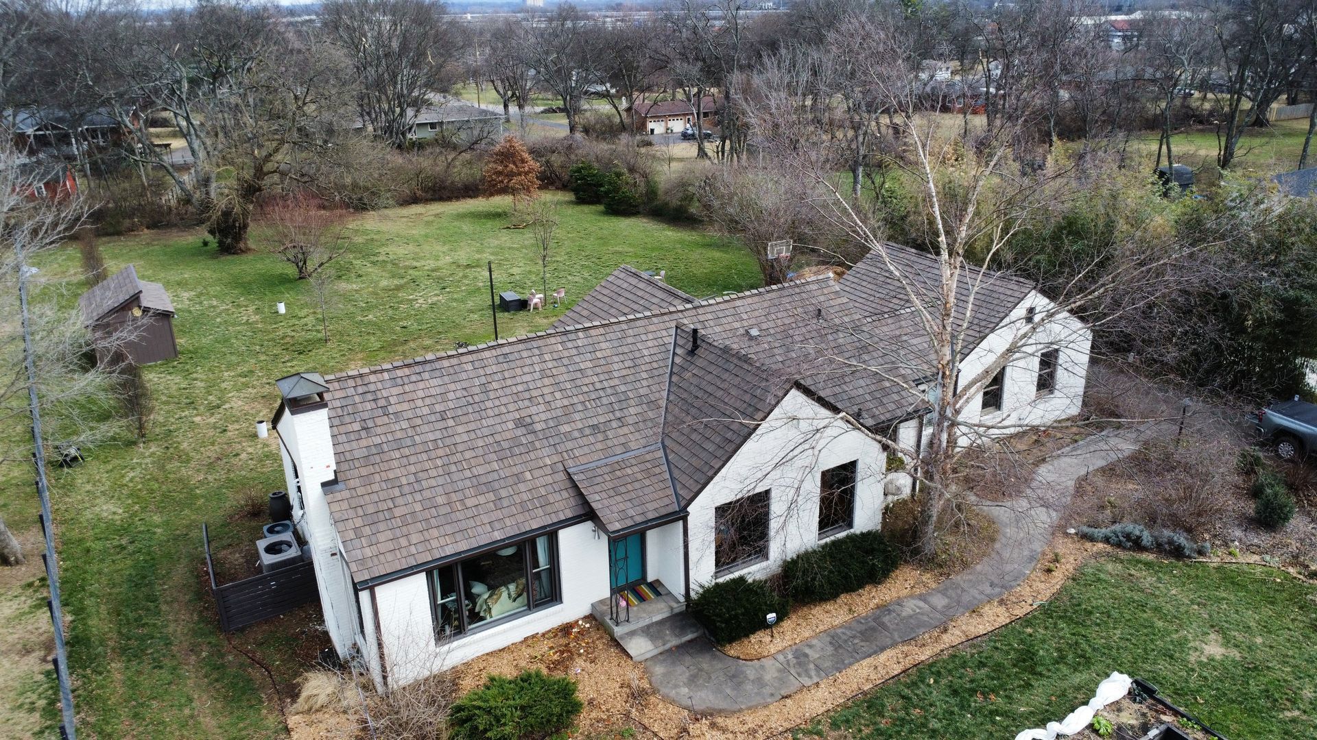 Aerial view of a white cottage with a gray roof, surrounded by trees and a grassy yard.