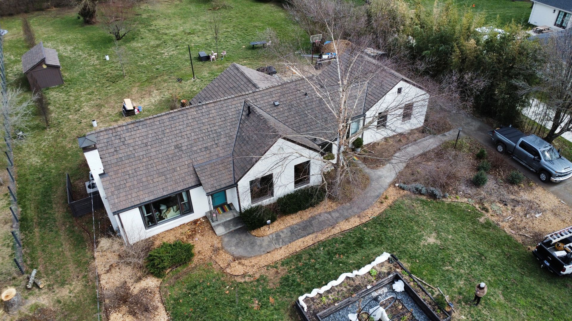 Aerial view of a white house with a brown roof, yard, and a parked car beside the driveway.