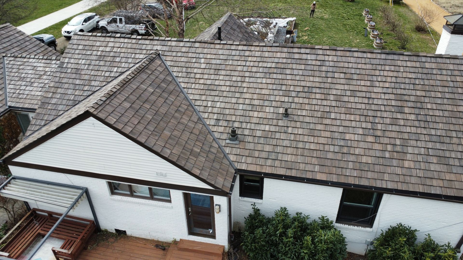 Aerial view of a white house with a gray shingle roof and attached garage, surrounded by greenery.