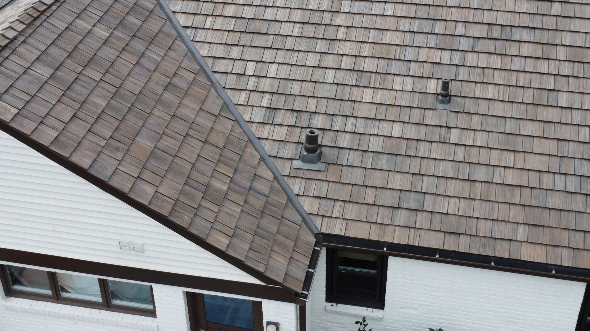 Two adjoining roofs with brown shingles and a white building facade below.