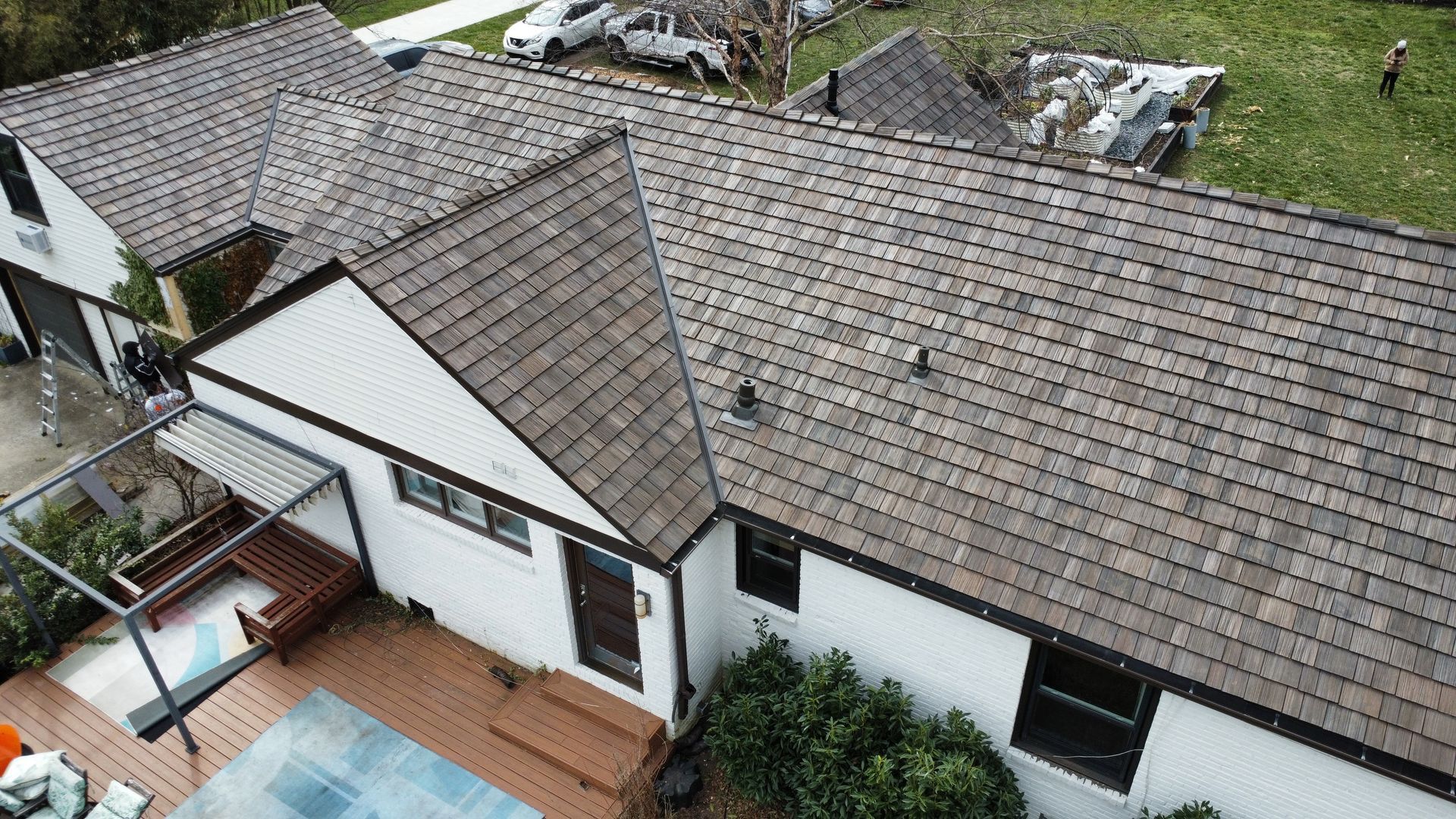 Aerial view of a white house with a gray shingle roof, deck, pool, and yard.