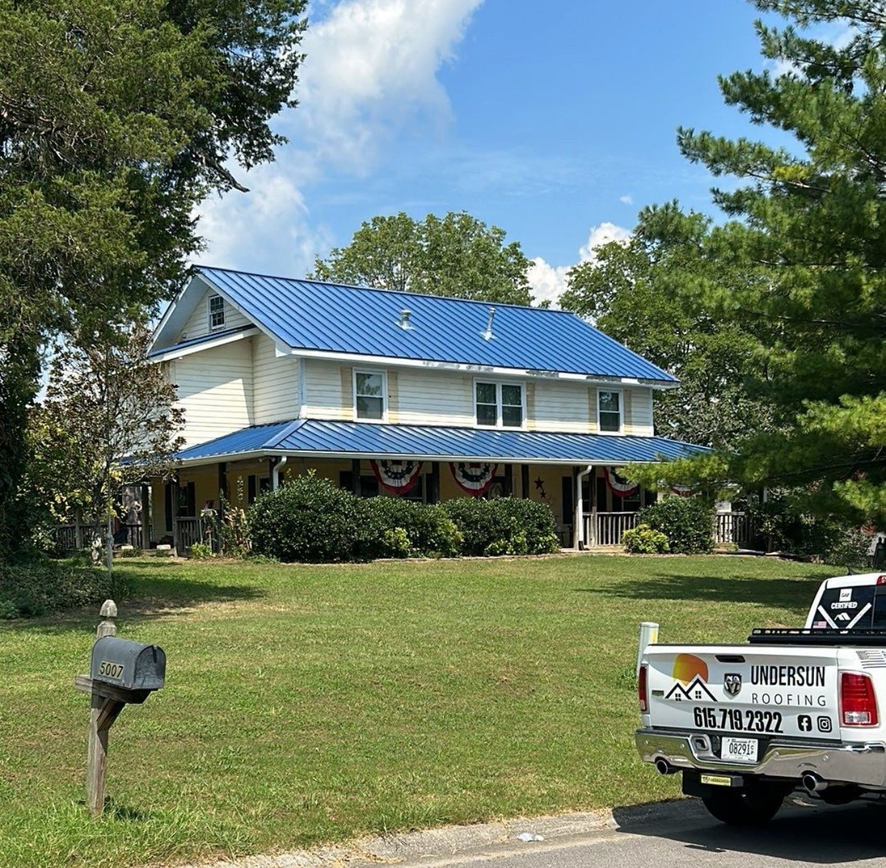 Two-story white house with blue roof and porch, set on a grassy lot beside a white pickup truck.