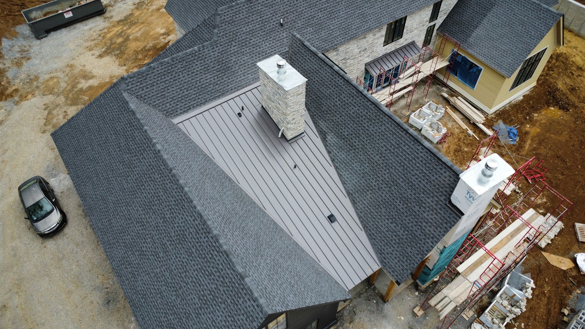 Aerial view of a house roof under construction with shingles, vents, and materials stacked nearby