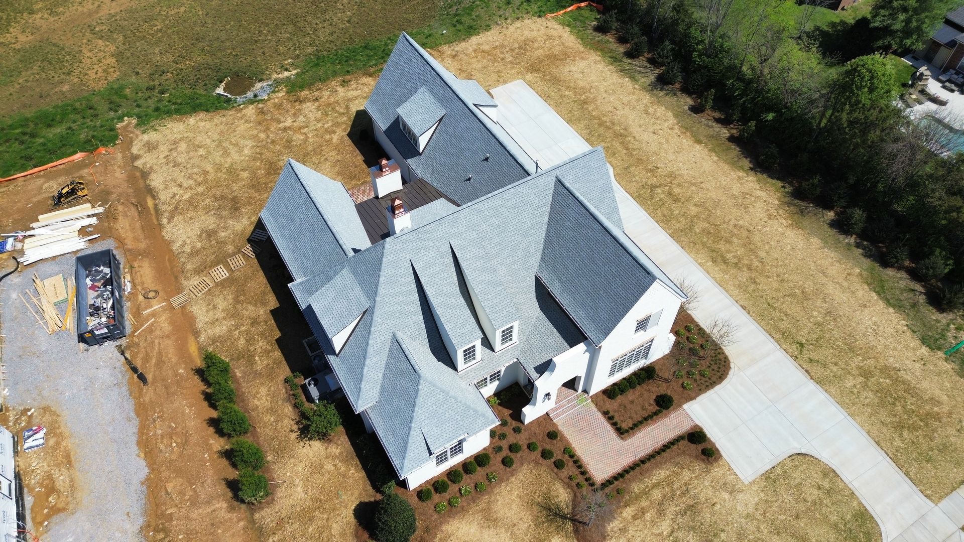 Aerial view of a white house with gray roof, driveway, and surrounding yard under construction.