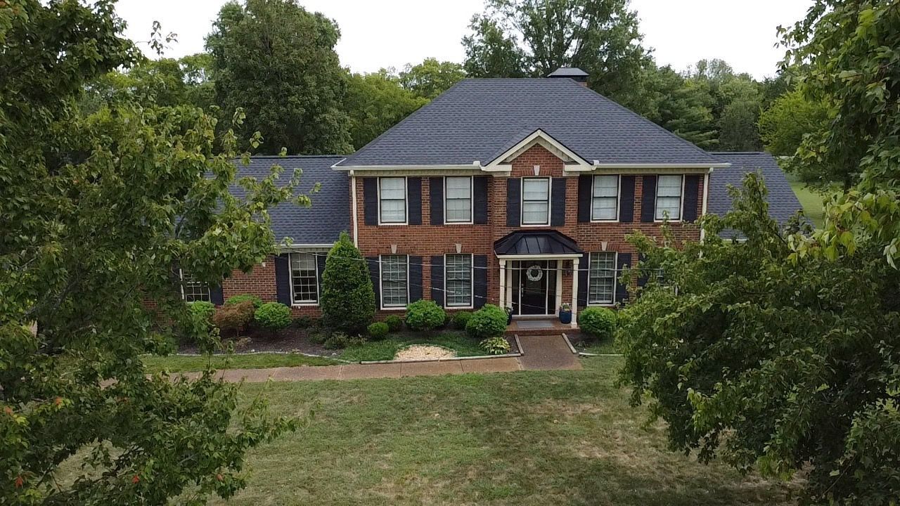 Two-story brick house with a dark roof, surrounded by trees and a grassy yard