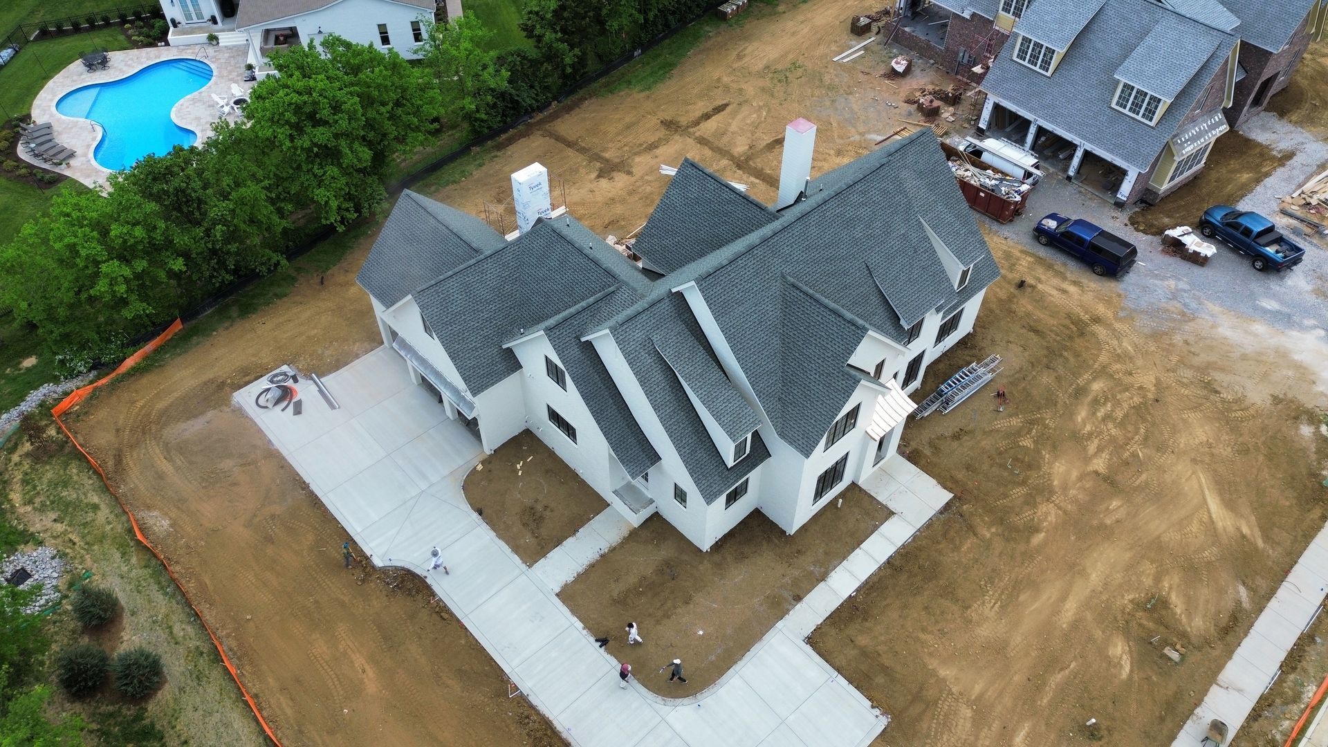 Aerial view of a large gray house with a white driveway and a blue backyard pool under construction or landscaping.