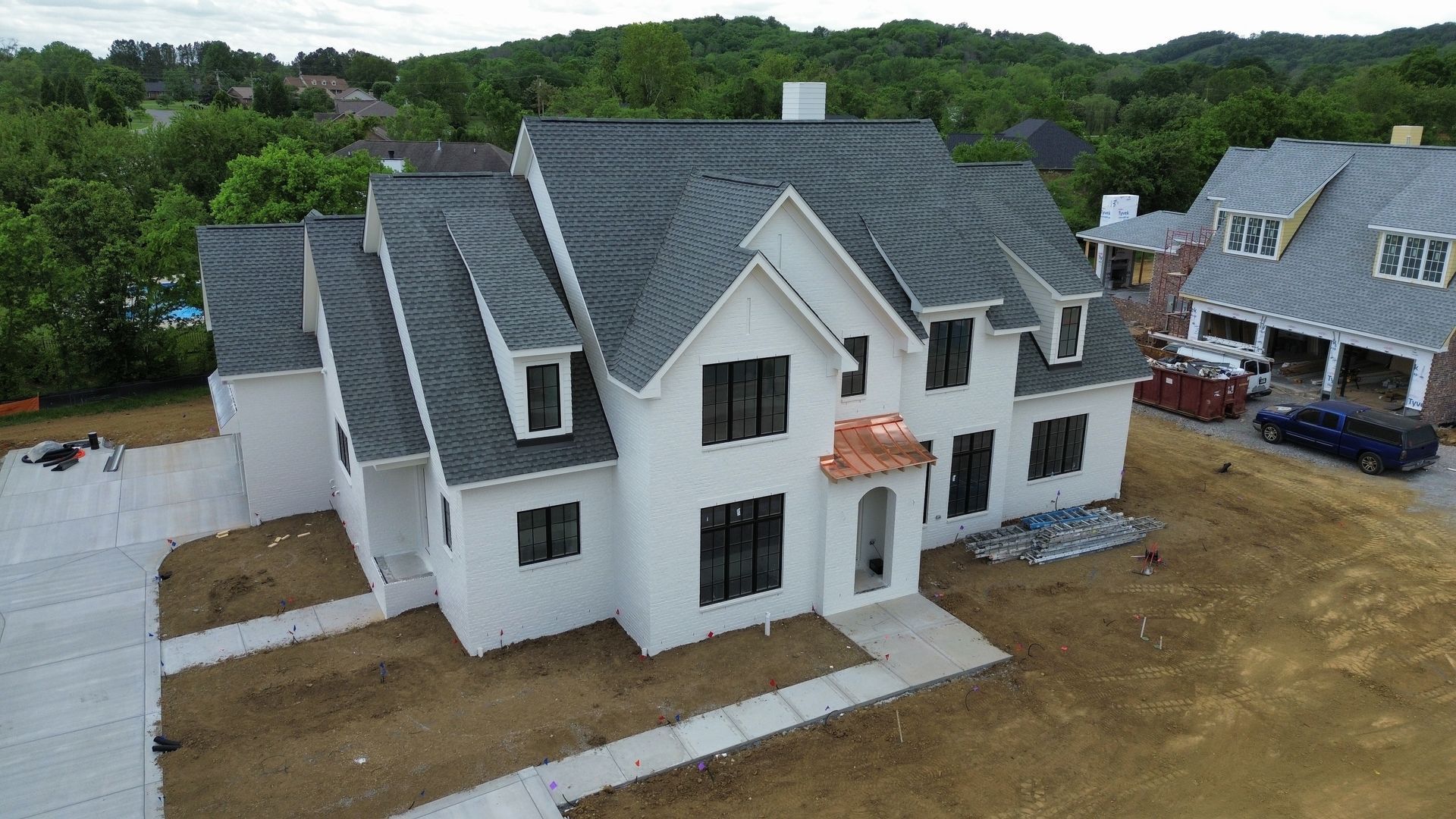 New white two-story house under construction with gray roof and unfinished yard
