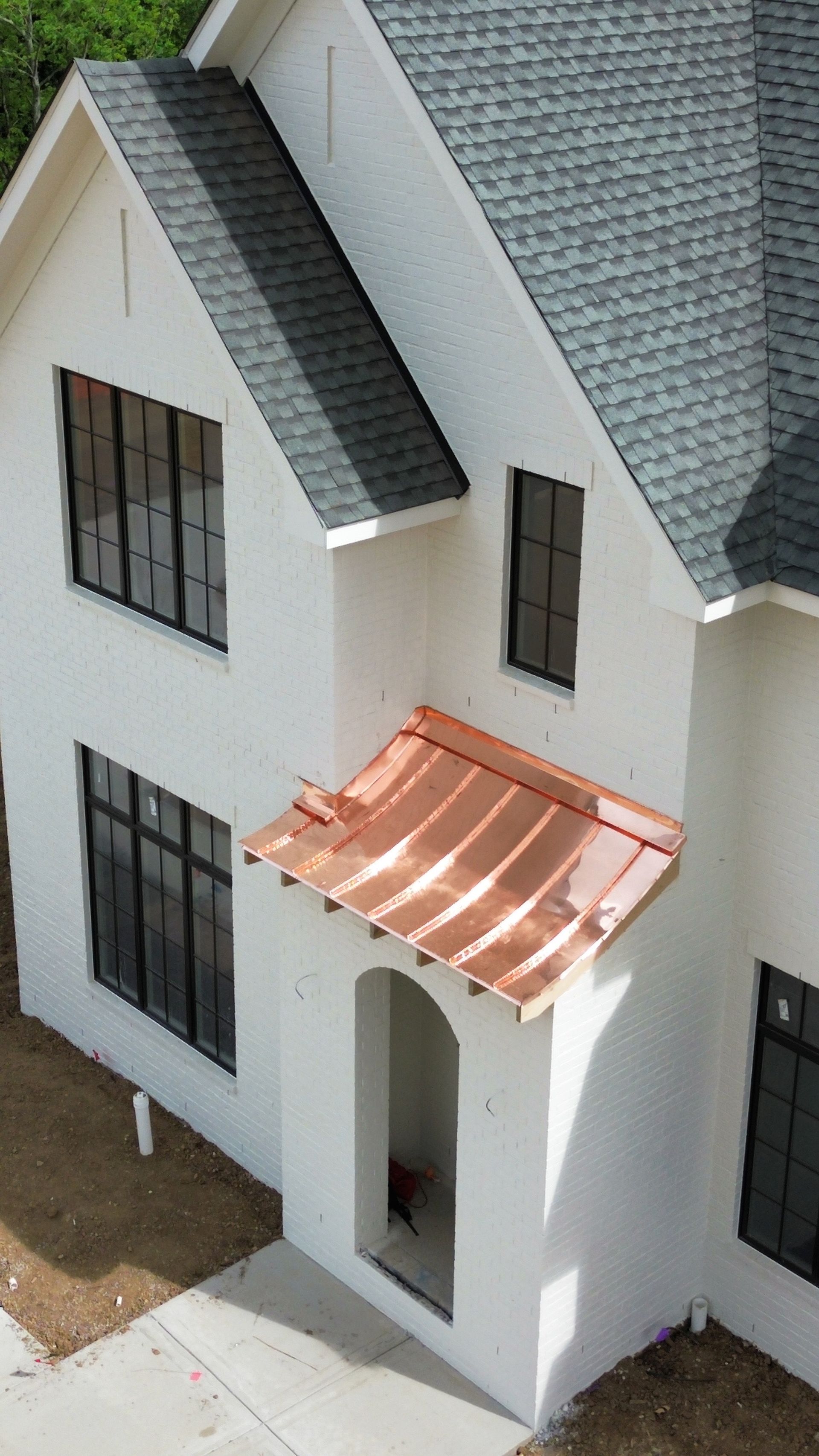 White two-story house with dark roof and black windows, featuring a copper awning over the front door.