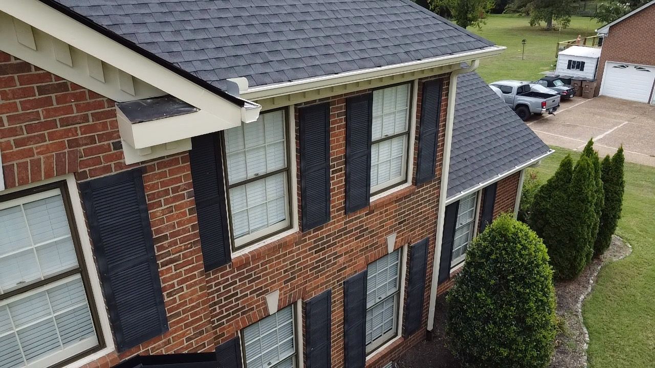 Two-story brick house with black shutters and gray roof viewed from above