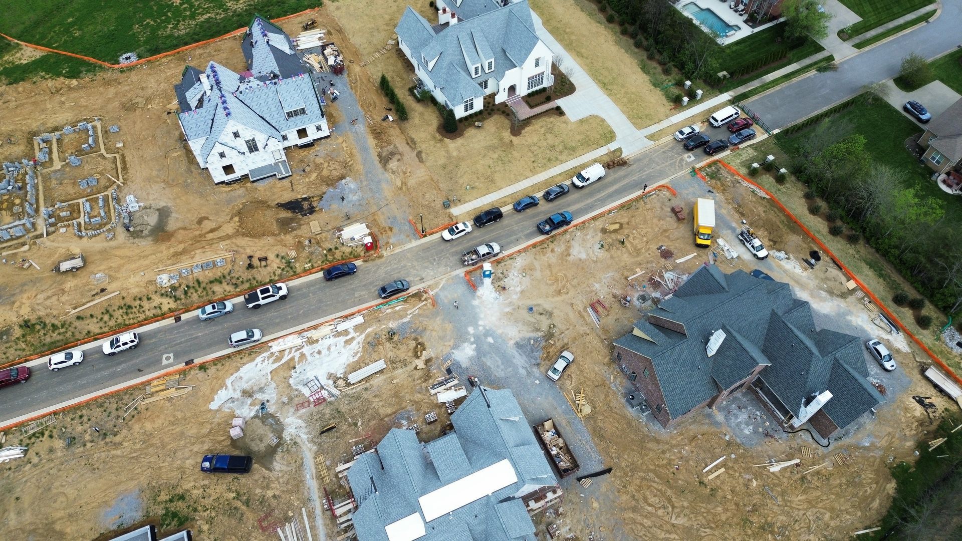 Aerial view of a flooded neighborhood with damaged houses, debris, and emergency vehicles on a road